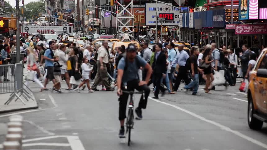 Traffic and pedestrians travel along a city street during the day