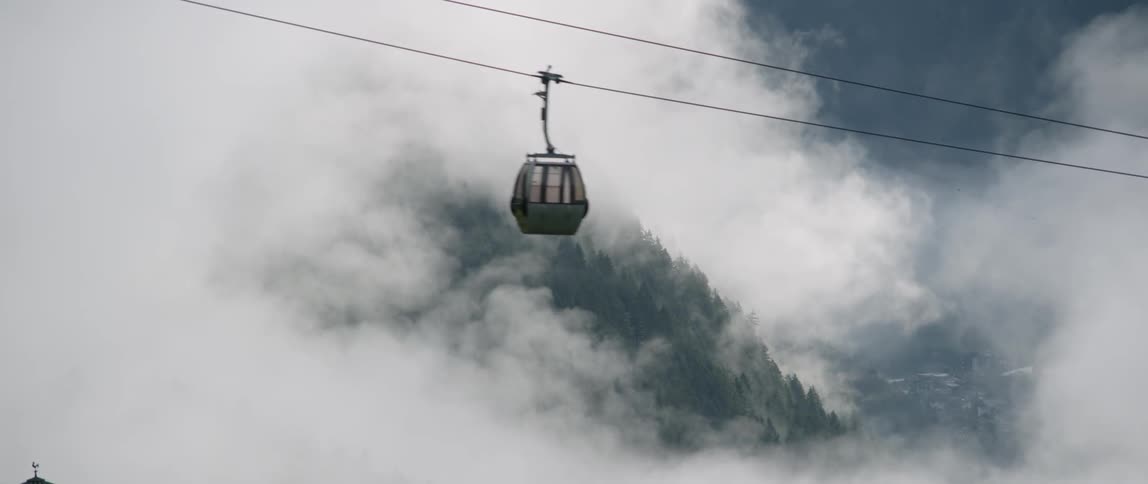 A gondola is running up an incline above a mountain on a cloudy day