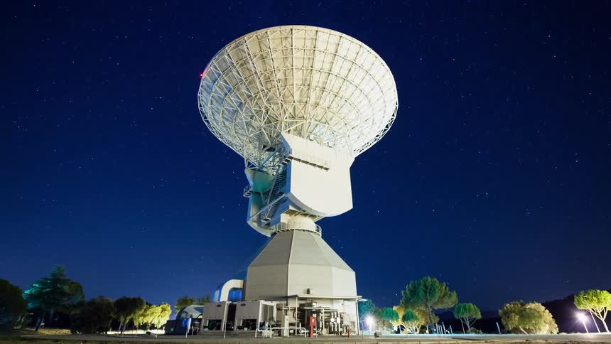 Stars move across the sky over a large satellite dish