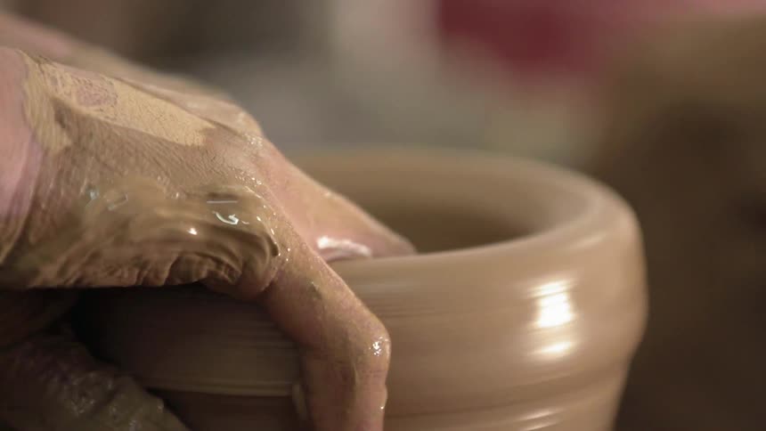 Hands shape a bowl on a pottery wheel