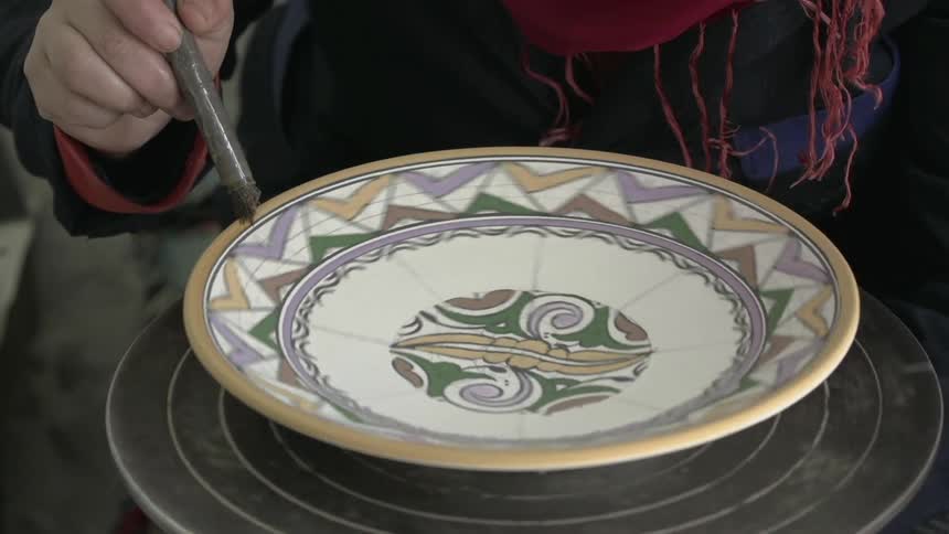 Person decorates a bowl that is spinning on a pottery wheel