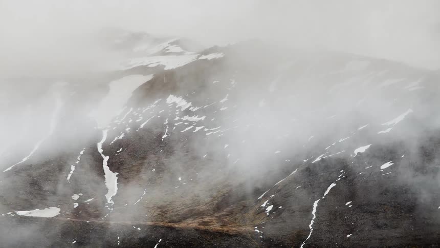 Fog and clouds move around a hill with snow trails