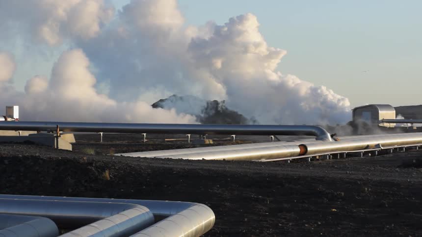 Steam is billowing from an industrial pipeline and plant during the day