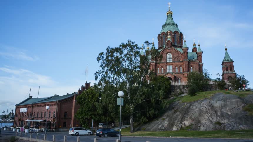 People and cars travel in front of a church on a hill