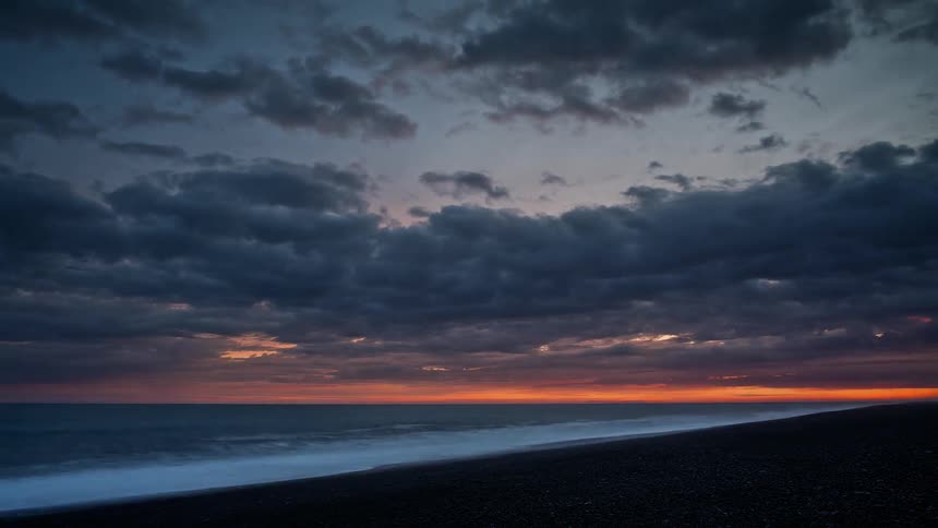 Clouds are moving out across a beach as dusk turns to night