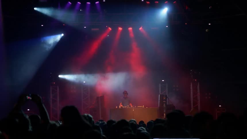 A dj is performing on a stage illuminated by flashing lights