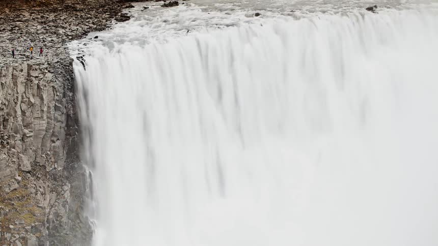 People walk on the rocks at the top of a waterfall