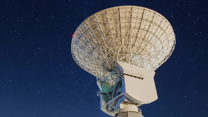 A radio satellite dish is pointed towards the stars at night