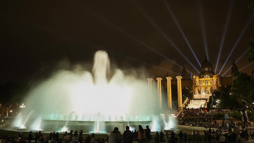 A water fountain is displaying colors and patterns at night in a public plaza