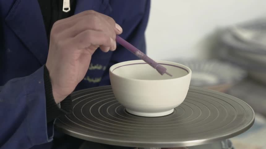 A person paints a bowl on a pottery wheel
