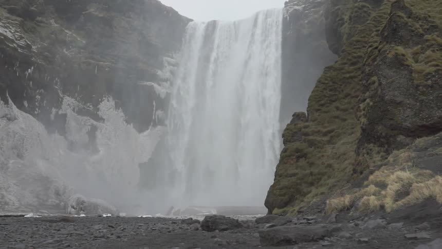A waterfall is cascading into a pool at the bottom of cliffs during the day