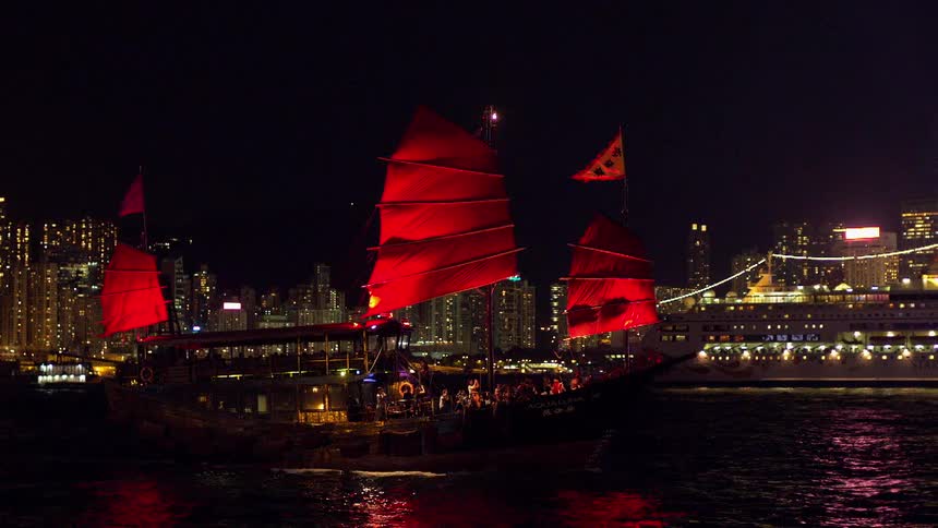 A boat floats near city skyscrapers at night