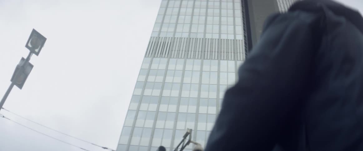 People are walking on the sidewalk below a skyscraper on a cloudy day