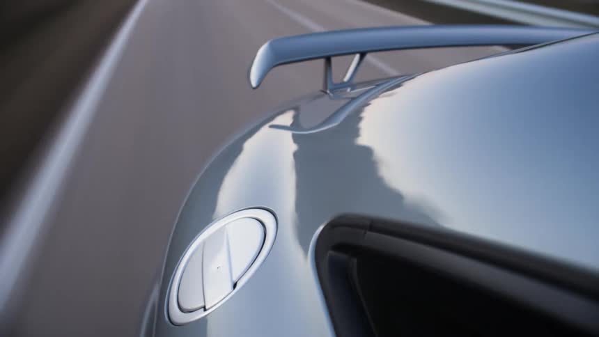 A car with a spoiler travels down a road to a dirt shoulder