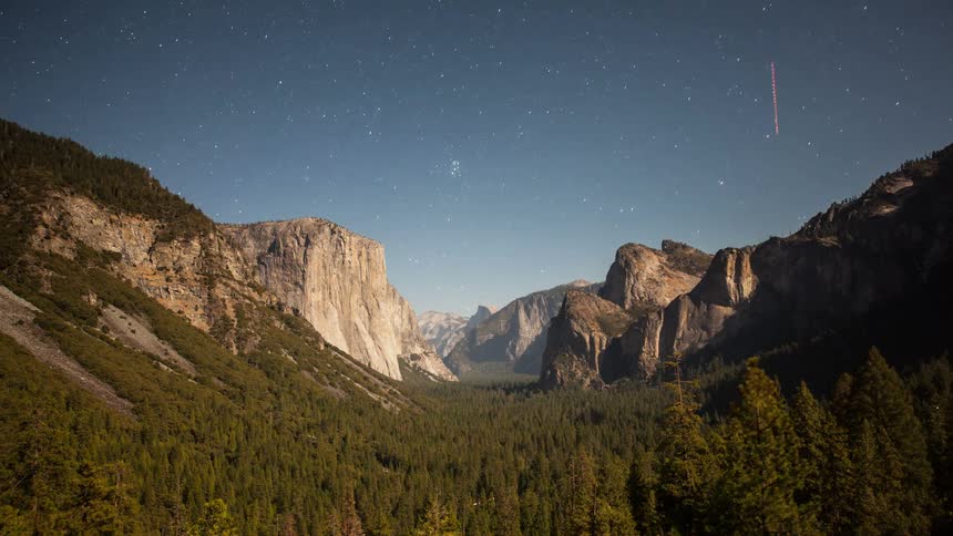 Stars swirl above a mountain forest