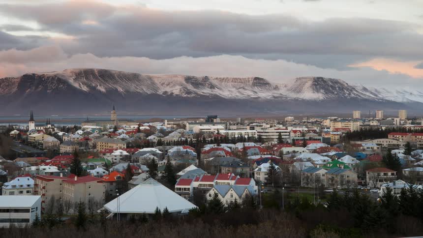 Storms clouds are moving over mountains and a town as dusk falls