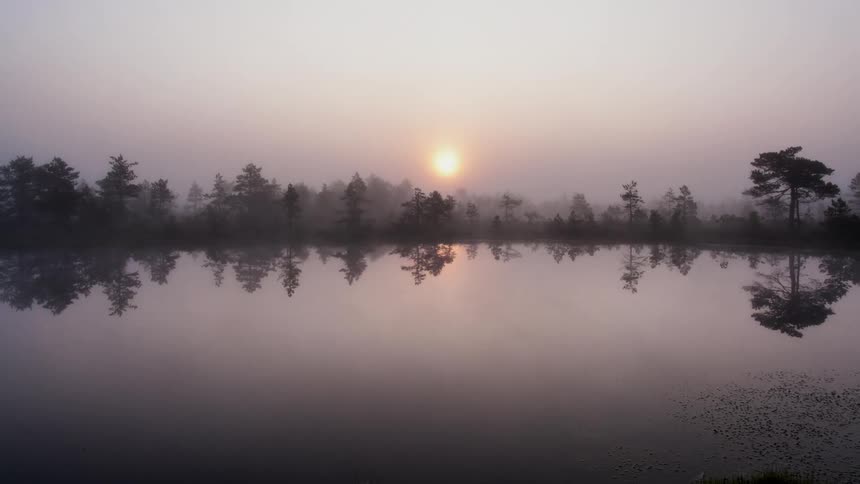 The sun rises as fog moves over the lake