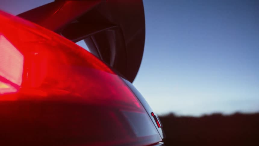 Scenery flashes by as a red car with a spoiler drives past