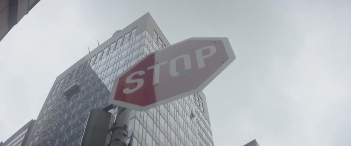 Someone walks beneath a stop sign near a skyscraper