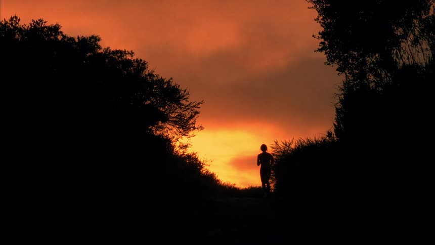 A woman jogs under orange sun glow