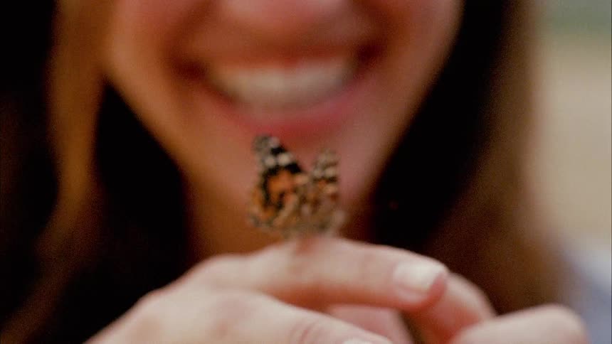 A woman smiles at the butterfly on her finger