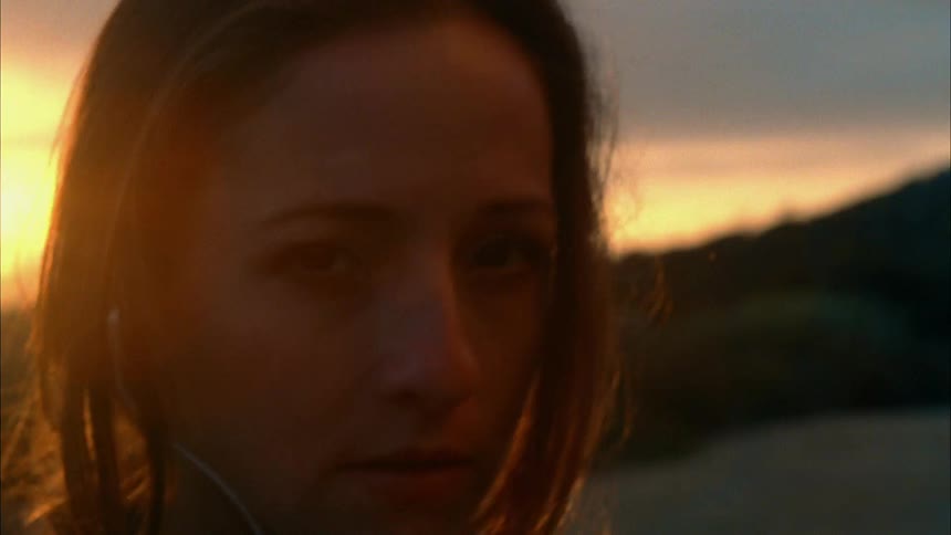 A woman looks sharply around as she stands outside at sunset