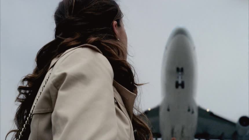A traveler watches a jet fly at an airport