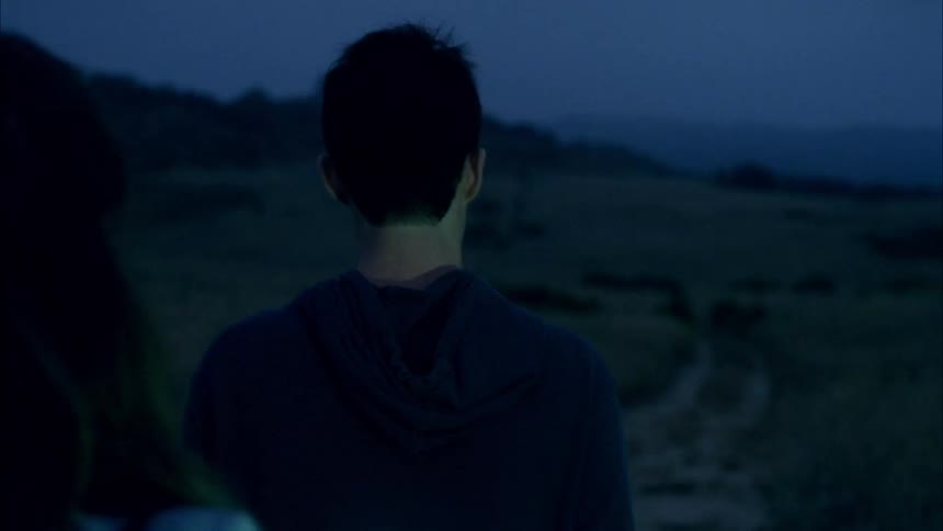 Young man and woman walk outdoors while using a flashlight to help guide them