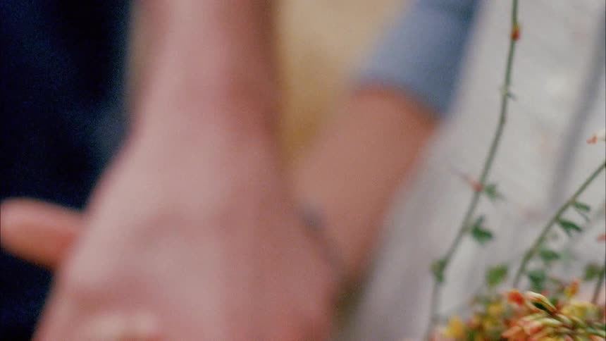 Two people hold hands and one person holds a bunch of flowers