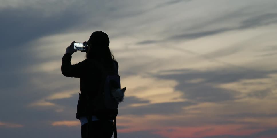 Woman takes picture with her phone outside at sunset