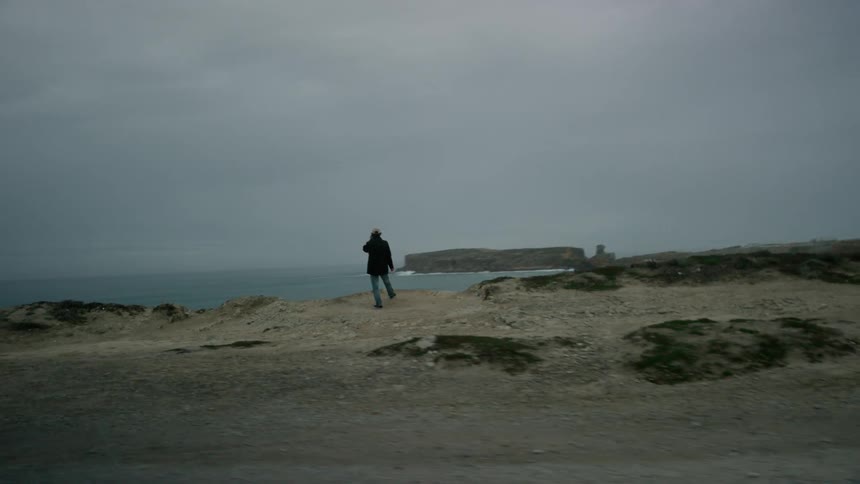 A person stands on a ridge overlooking the ocean on a cloudy day