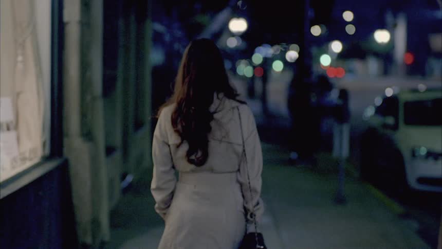 Woman walks on a sidewalk past a shop in a city at night