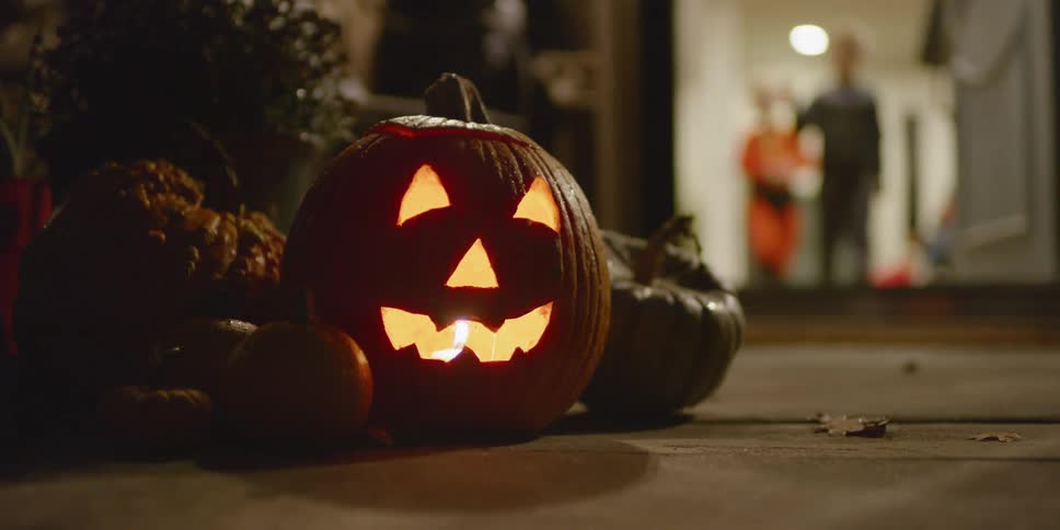 A jack o lantern and other gourds sit on a patio at night