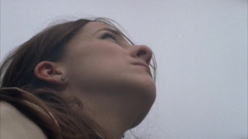 A woman is watching a plane fly overhead on a cloudy day