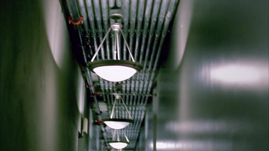 Lights hanging from a ceiling inside a hallway are casting shadows and reflections on the walls