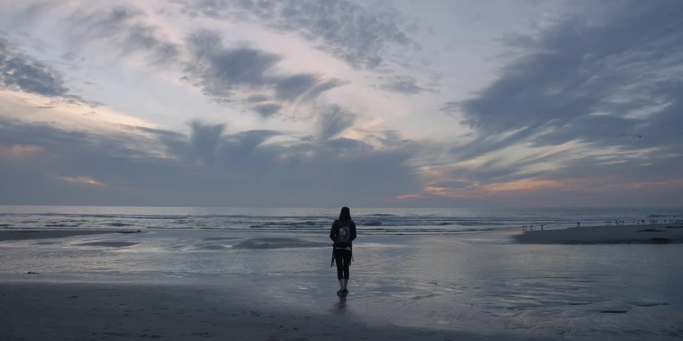 A person stands on the beach watching the sunset