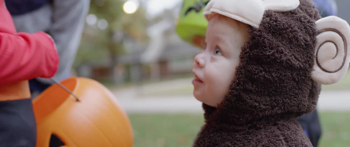 A toddler in a costume is holding a treat outside on halloween