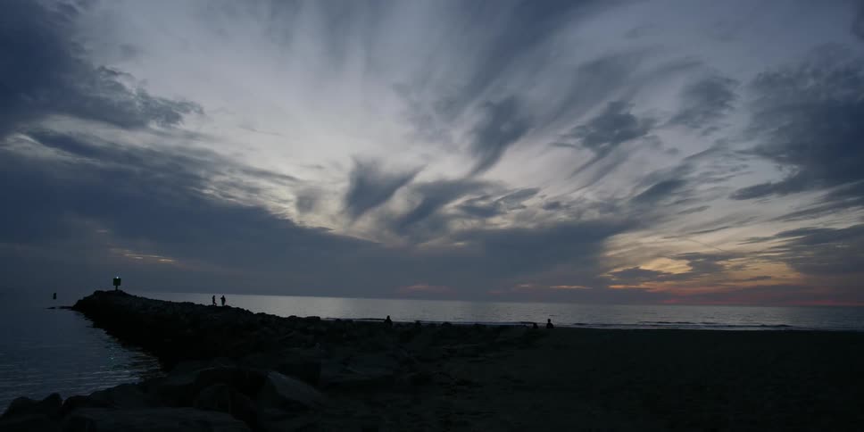 People are walking on a jetting under cloudy skies at dusk