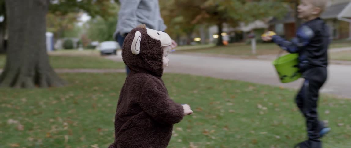 A toddler in a costume is running on a lawn outside on halloween