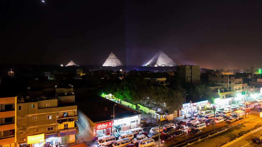 Cars drive on a city street with pyramids in the distance