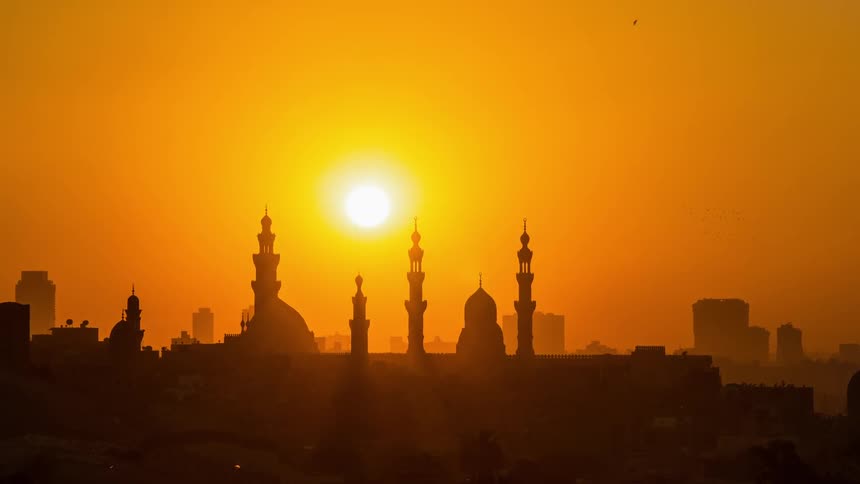 The sun shines on ornate buildings with an orange glow