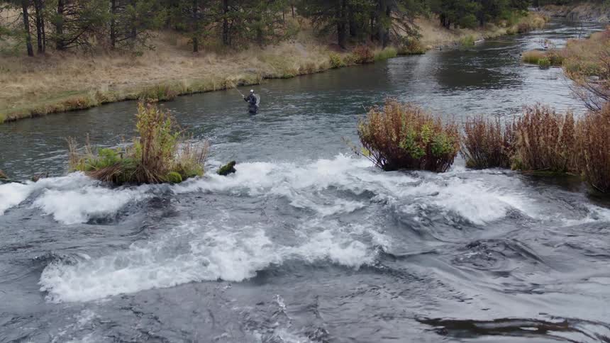 A man stands waist deep in water while fly fishing