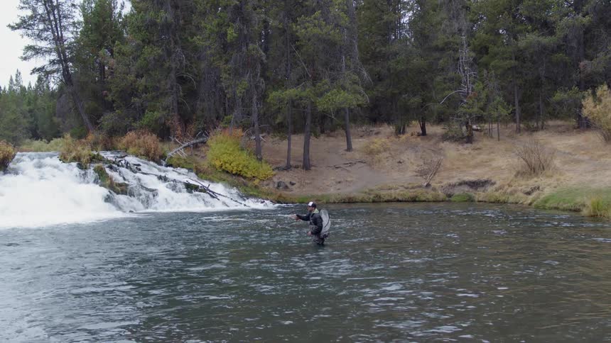 A man is standing in the middle of a stream fly fishing