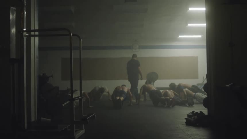 A coach has some people doing push ups on the ground of a gym