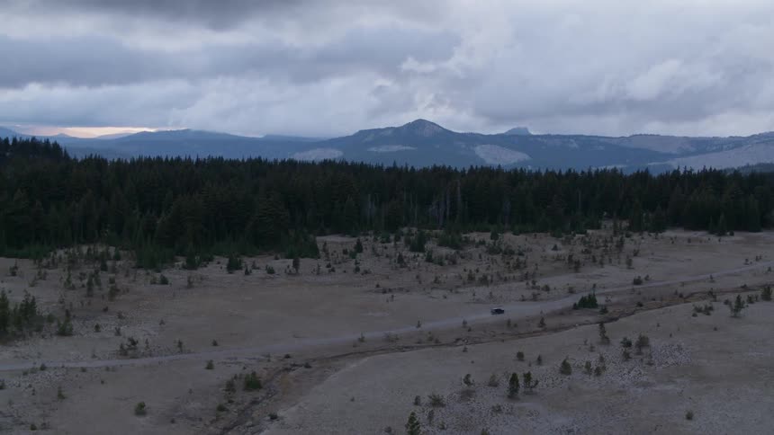 A vehicle drives by forest trees and mountains