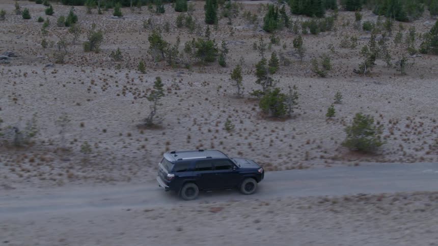 A vehicle drives on a dirt forest road