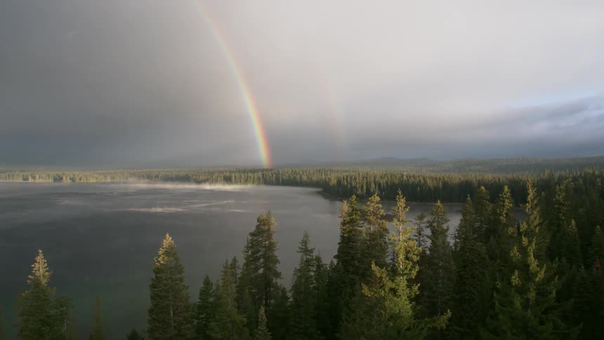 A rainbow extends above a forest and lake