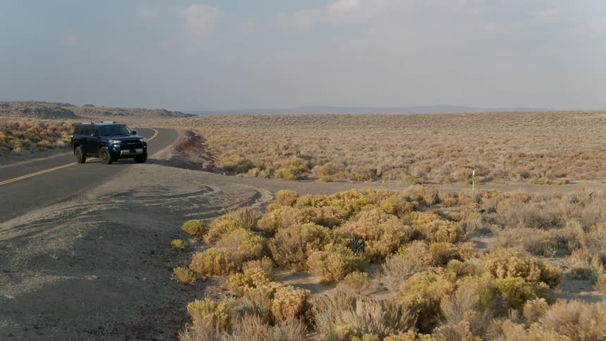 An suv is turning off a highway onto a dirt road in a desert landscape during the day