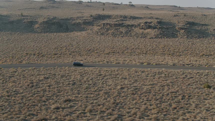 A vehicle drives on a rural desert road