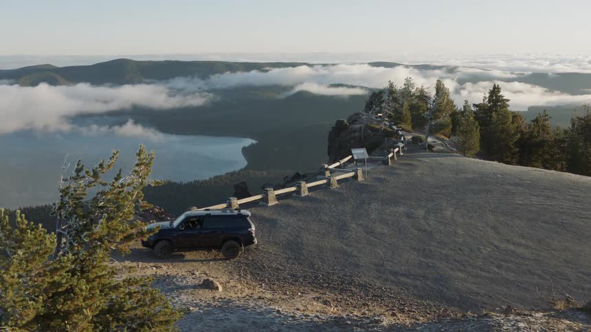 An suv is parked at a viewpoint above the clouds during the day